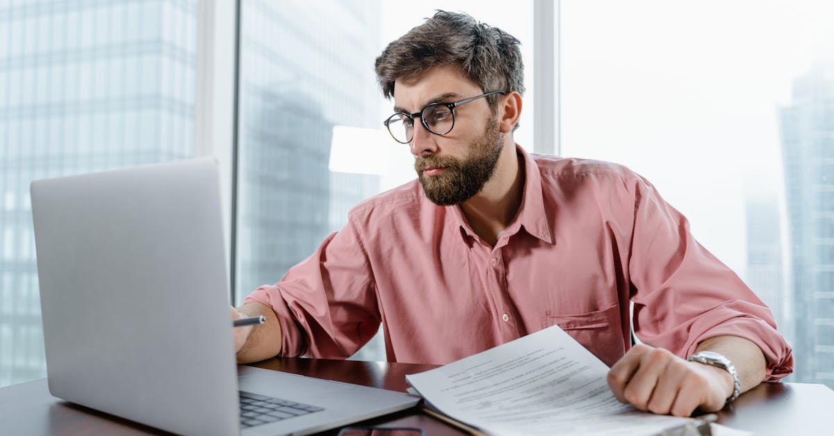 A businessman in an office reviews documents and data on a laptop, concentrating on financial analysis.